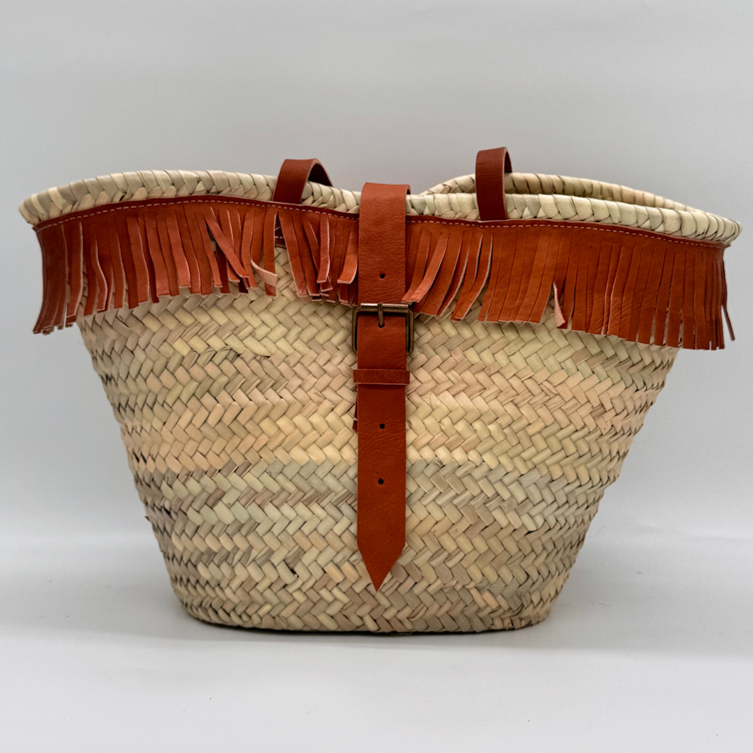 Handgewebte Basttasche aus Naturstroh mit braunen Lederfransen am oberen Rand und verstellbarem Lederriemen als Verschluss