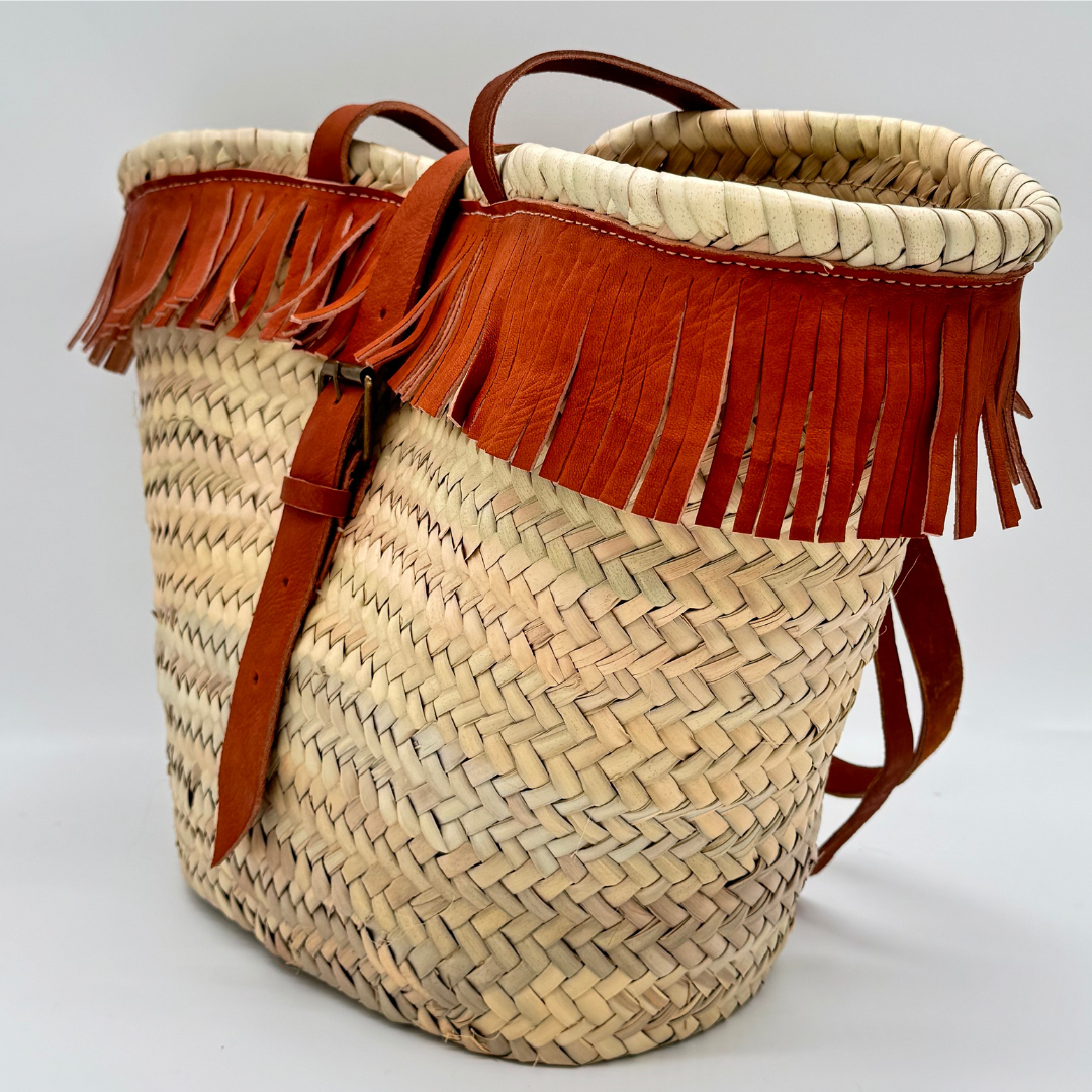 Handgewebte Basttasche aus Naturstroh mit braunen Lederfransen am oberen Rand und verstellbarem Lederriemen als Verschluss