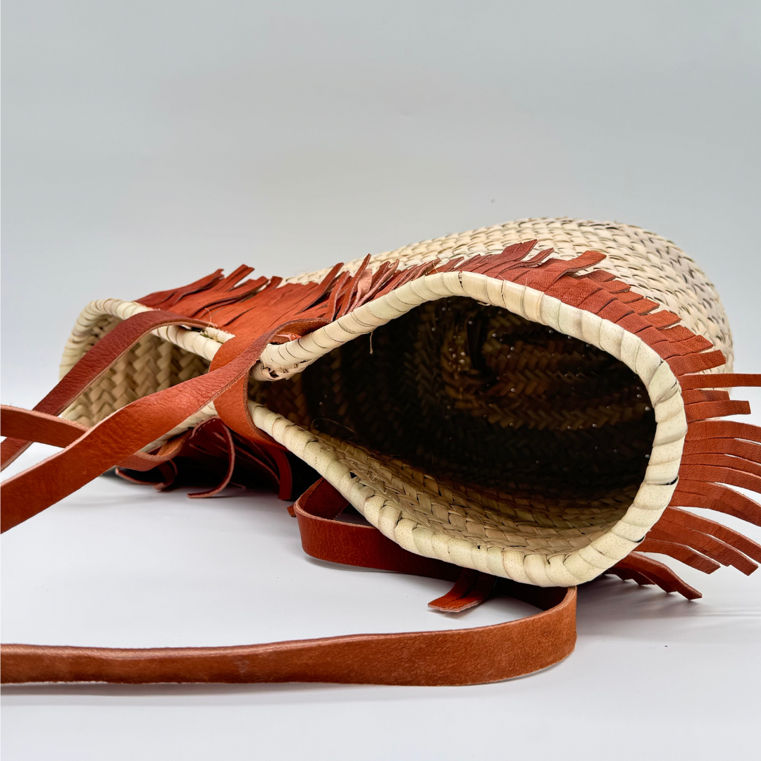 Handgewebte Basttasche aus Naturstroh mit braunen Lederfransen am oberen Rand und verstellbarem Lederriemen als Verschluss
