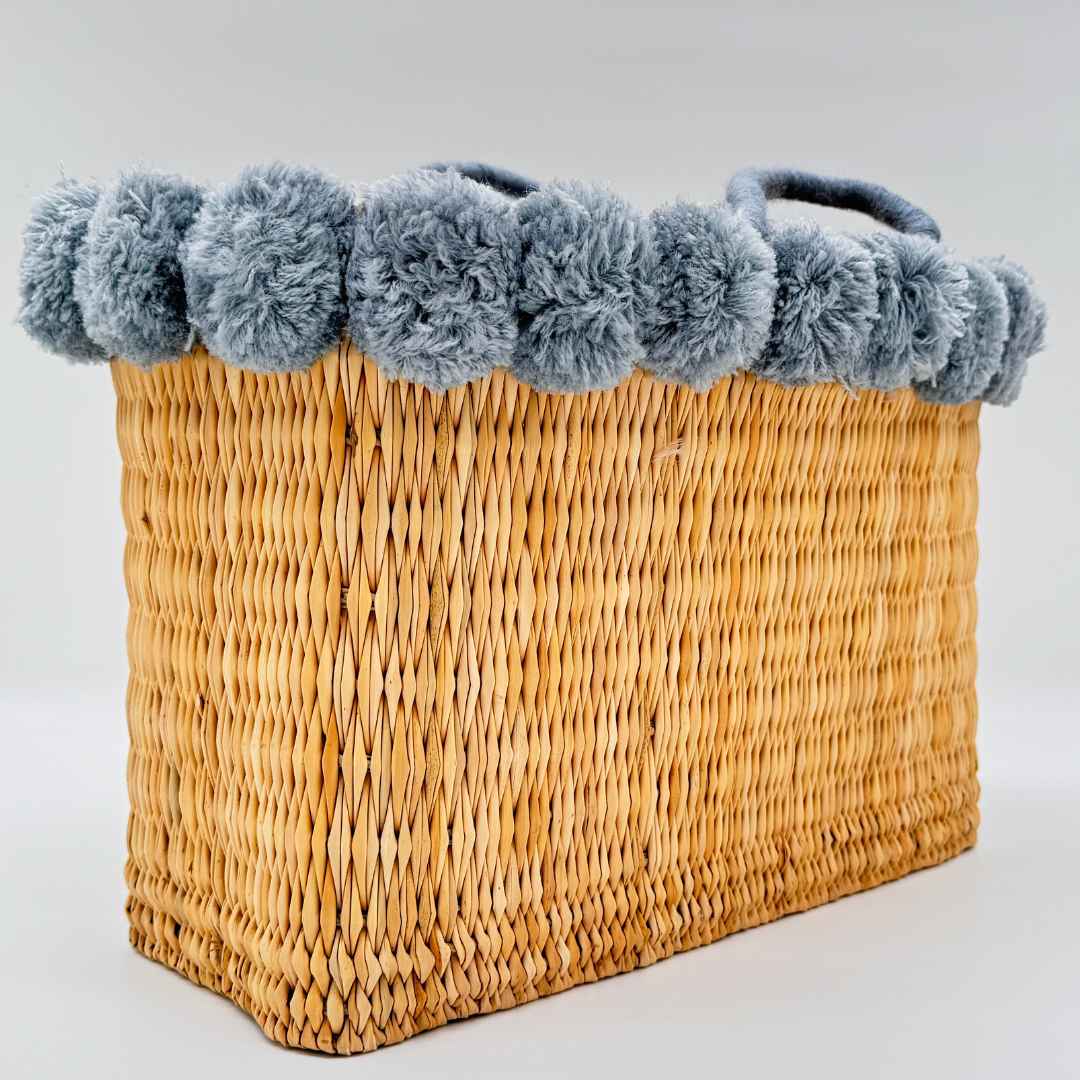 Handgewebte rechteckige Basttasche aus Naturstroh mit grauen Pompons am oberen Rand und kurzen Schlaufen aus Bast