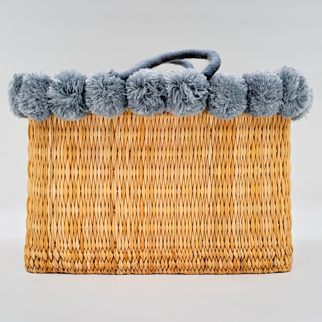 Handgewebte rechteckige Basttasche aus Naturstroh mit grauen Pompons am oberen Rand und kurzen Schlaufen aus Bast