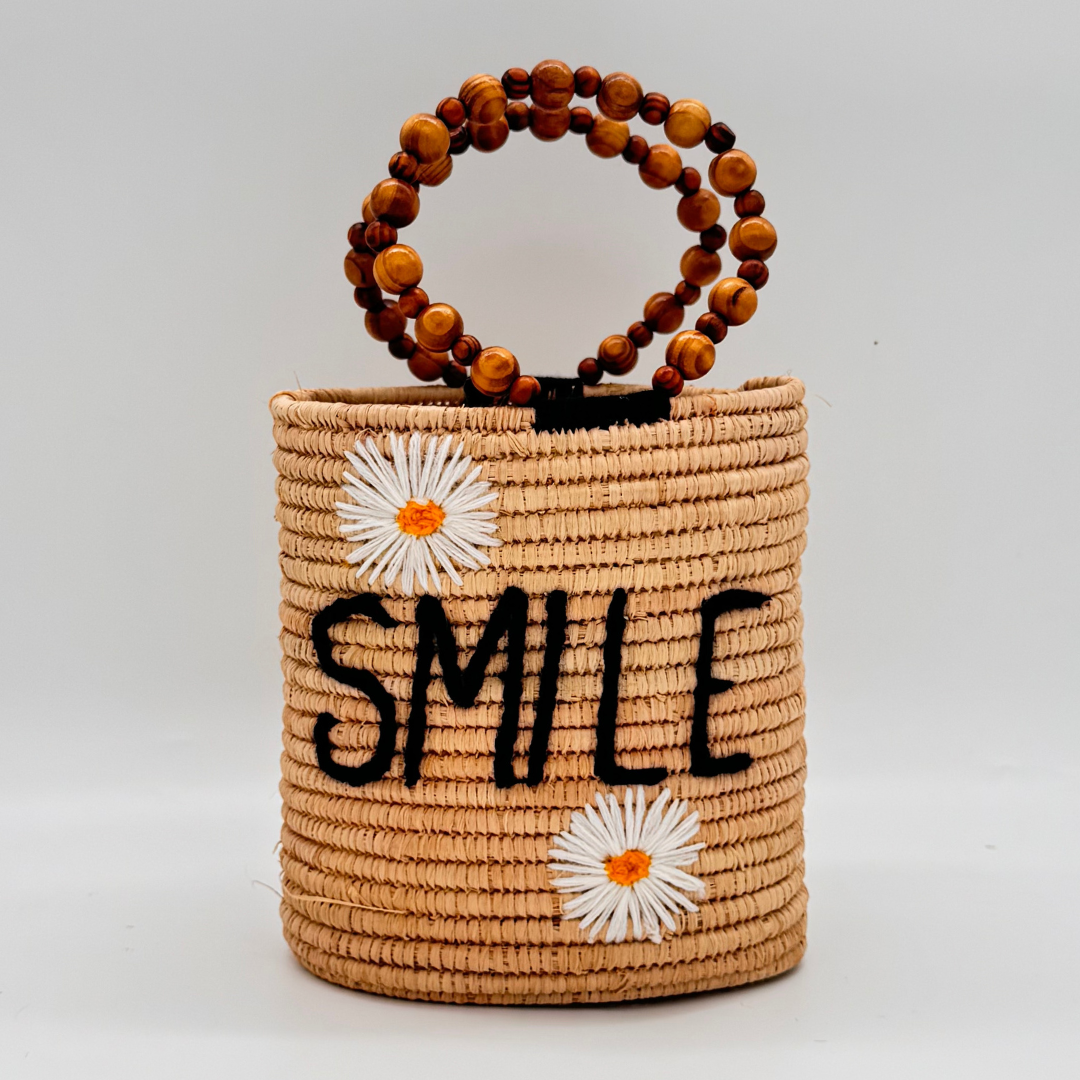 Handgewebte zylindrische Basttasche mit schwarzem ‚SMILE‘-Schriftzug, weißen Gänseblümchen-Applikationen und runden Holzperlen-Henkel