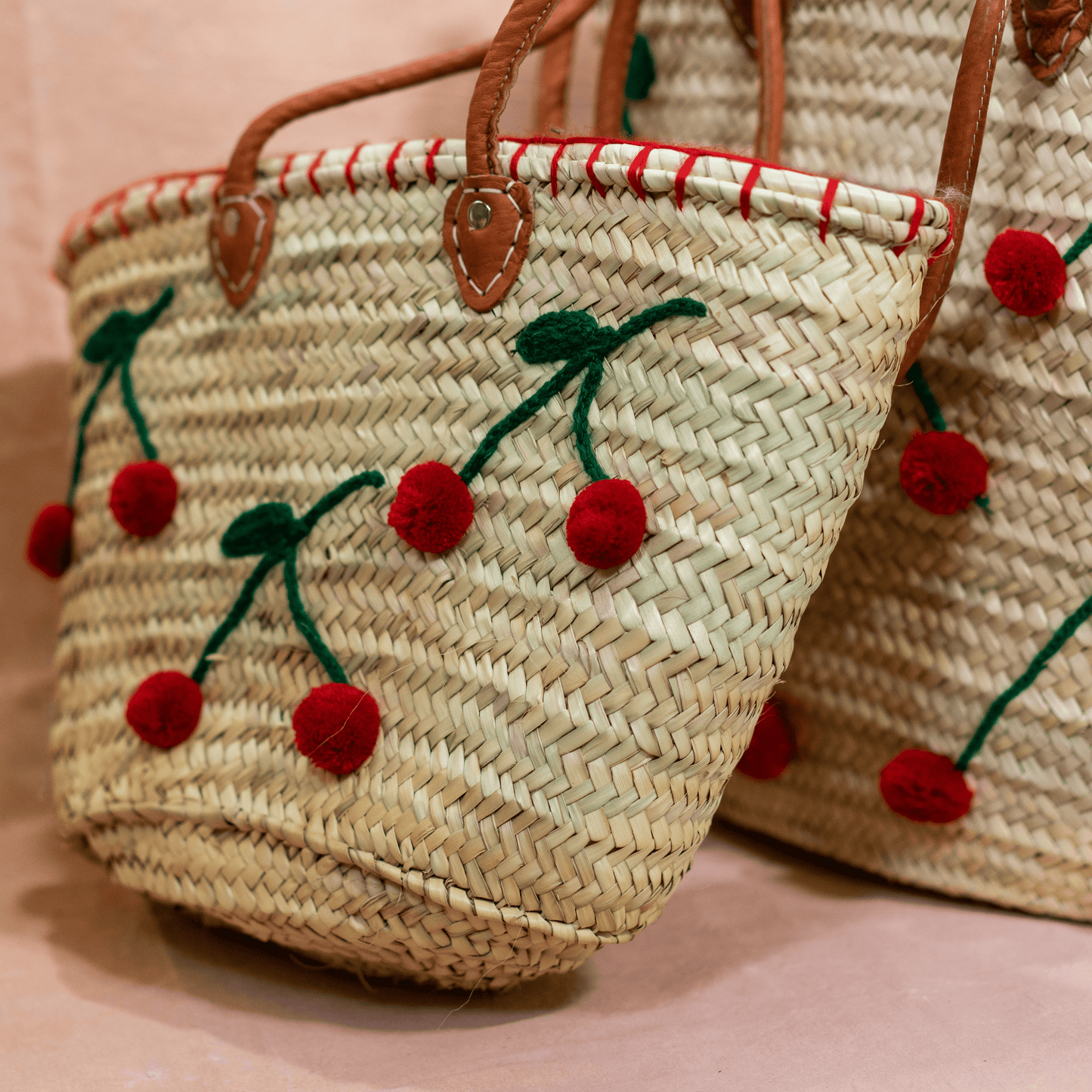 Handgewebte Basttasche aus Naturstroh mit grünen Garnstielen und roten Pompon-Kirschen sowie braunen Lederhenkeln