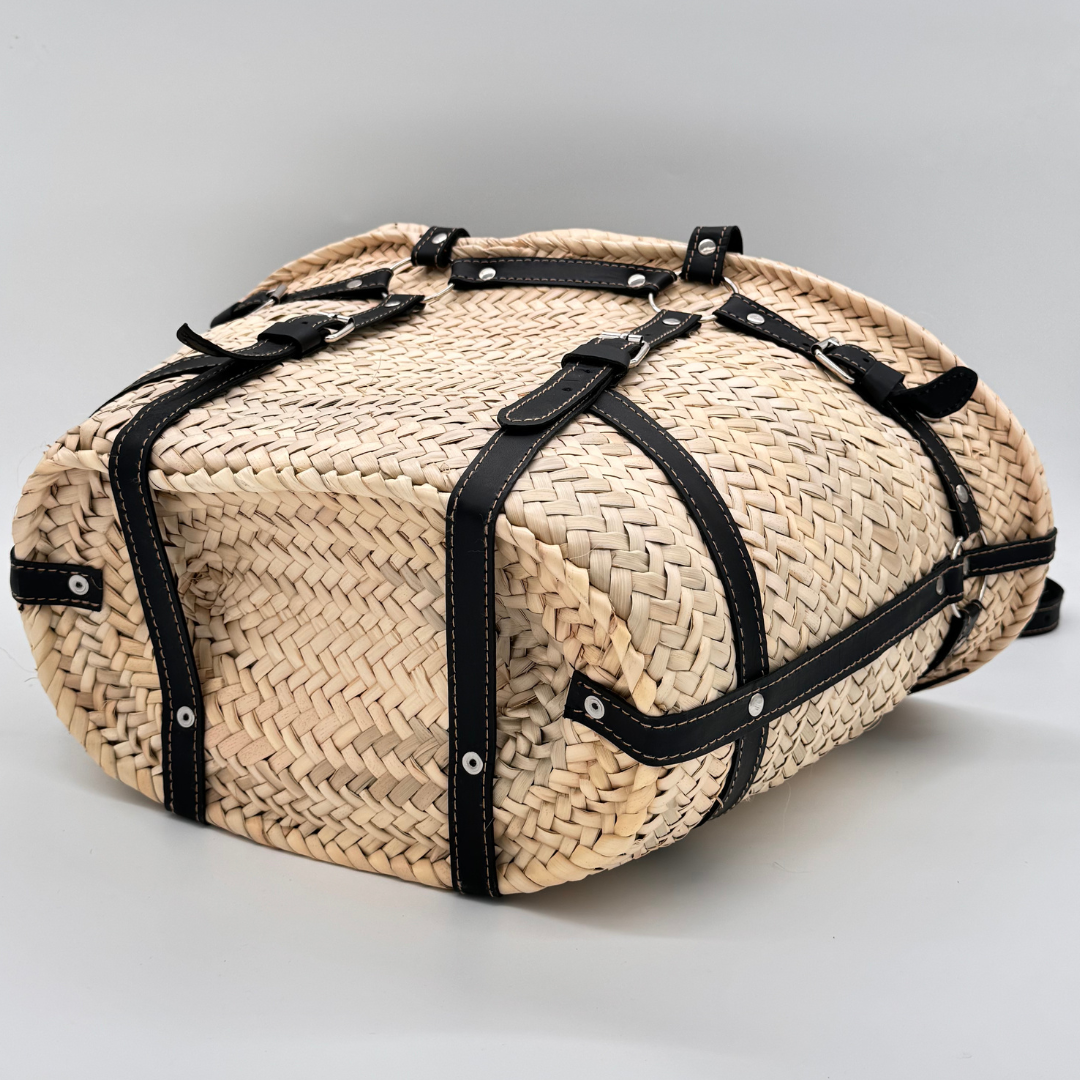 Handgewebte Strohtasche aus naturfarbenem Palmstroh mit schwarzen Lederriemen und silbernen Schnallen als dekorative Gürteldetails