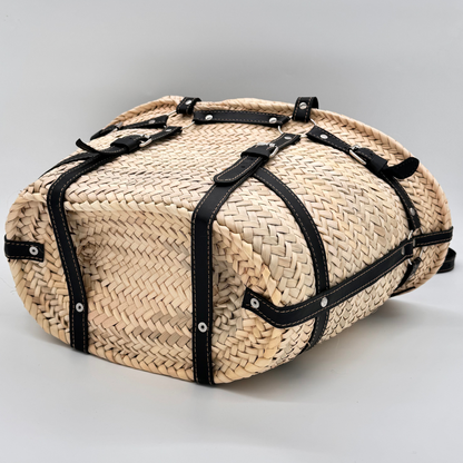 Handgewebte Strohtasche aus naturfarbenem Palmstroh mit schwarzen Lederriemen und silbernen Schnallen als dekorative Gürteldetails