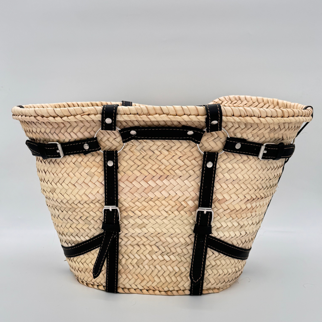 Handgewebte Strohtasche aus naturfarbenem Palmstroh mit schwarzen Lederriemen und silbernen Schnallen als dekorative Gürteldetails