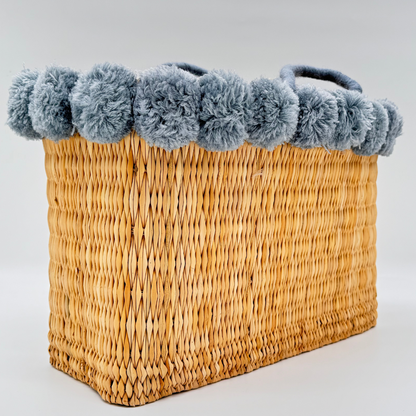Handgewebte rechteckige Basttasche aus Naturstroh mit grauen Pompons am oberen Rand und kurzen Schlaufen aus Bast