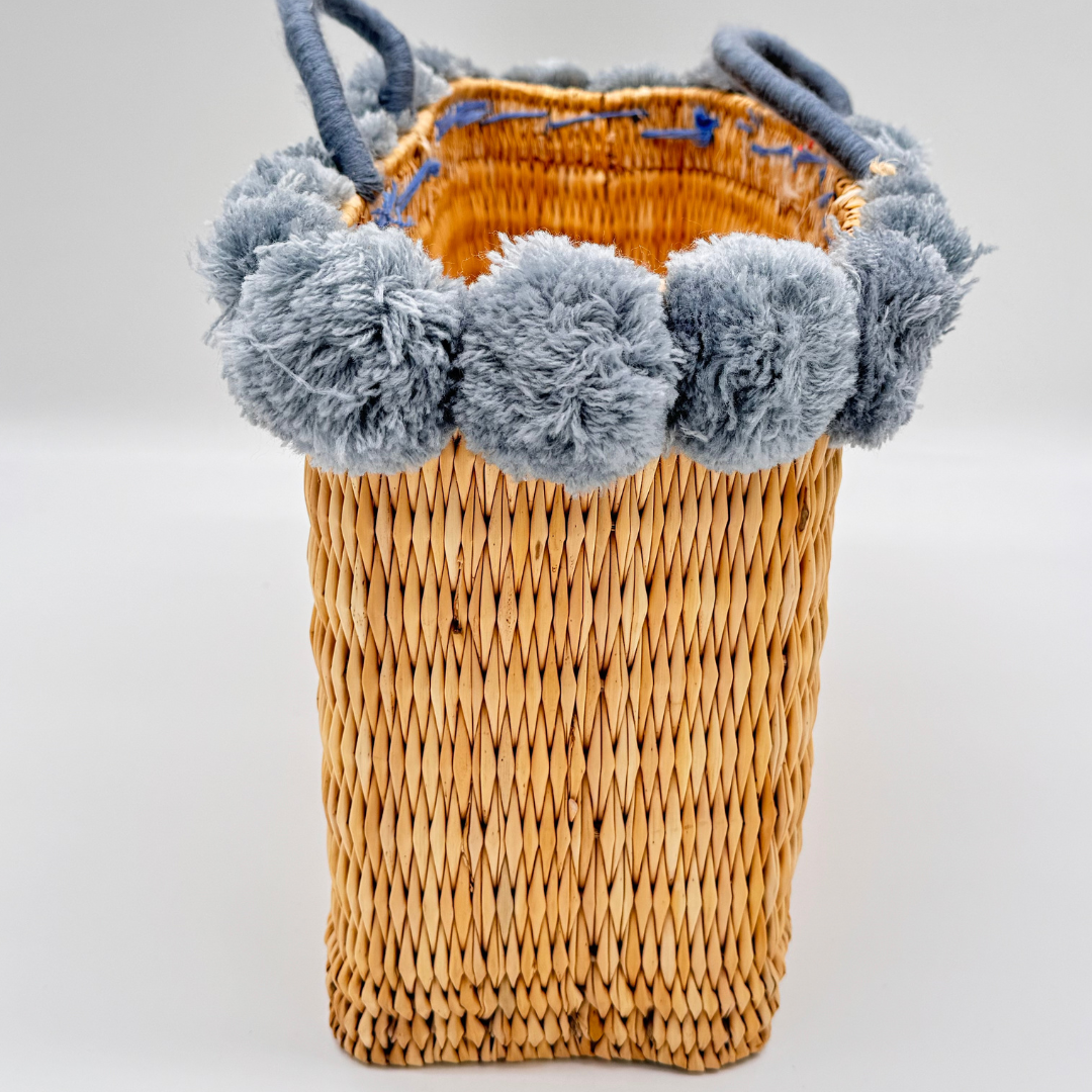 Handgewebte rechteckige Basttasche aus Naturstroh mit grauen Pompons am oberen Rand und kurzen Schlaufen aus Bast