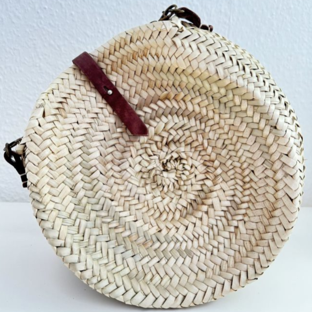 Runde, handgewebte Basttasche aus Palmstroh mit verstellbarem, schmalem braunem Lederriemen als Schultergurt