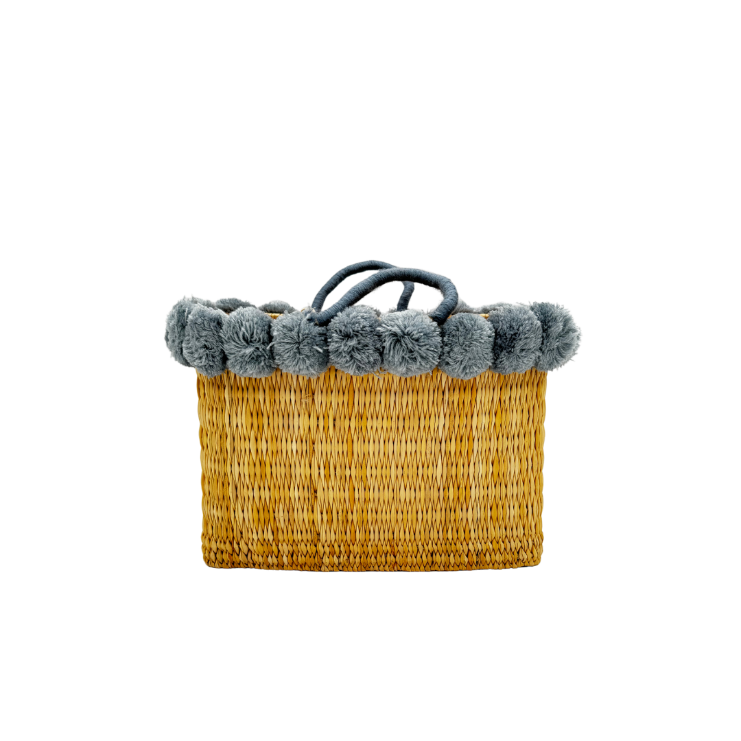 Handgewebte rechteckige Basttasche aus Naturstroh mit grauen Pompons am oberen Rand und kurzen Schlaufen aus Bast