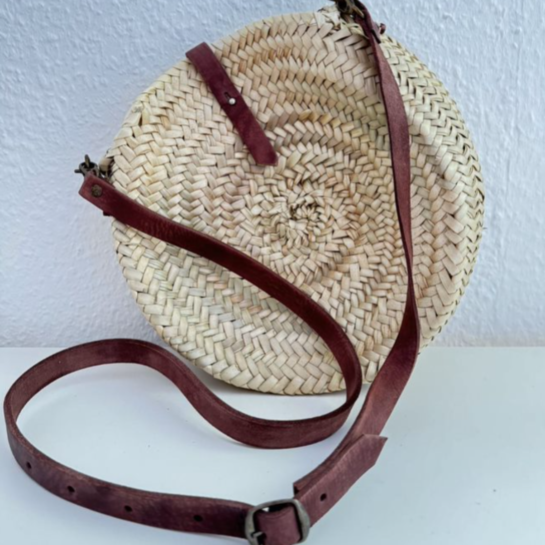 Runde, handgewebte Basttasche aus Palmstroh mit verstellbarem, schmalem braunem Lederriemen als Schultergurt