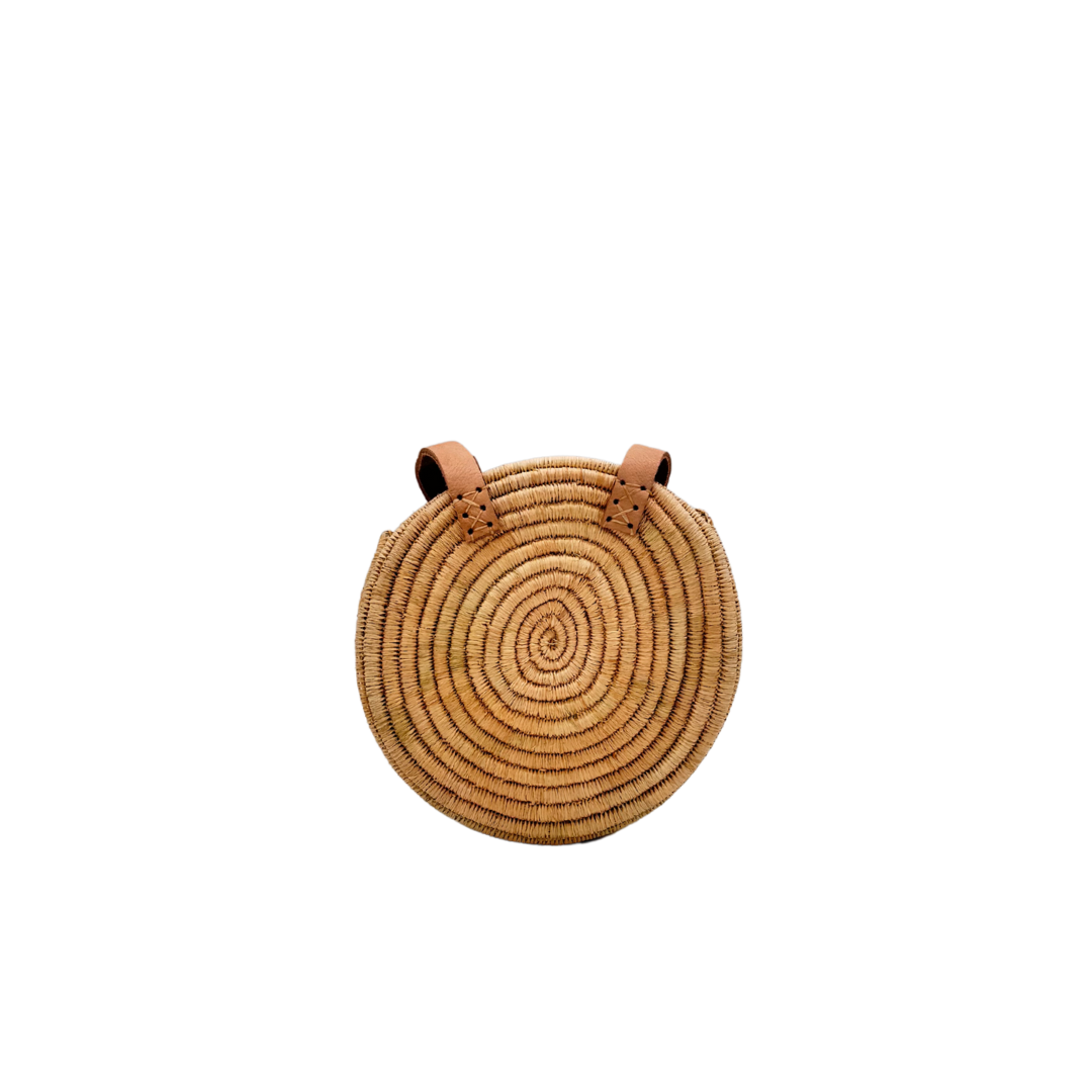 Kleine, runde Basttasche aus handgewebtem Raffia mit zwei braunen Lederlaschen zur Befestigung eines Trageriemens