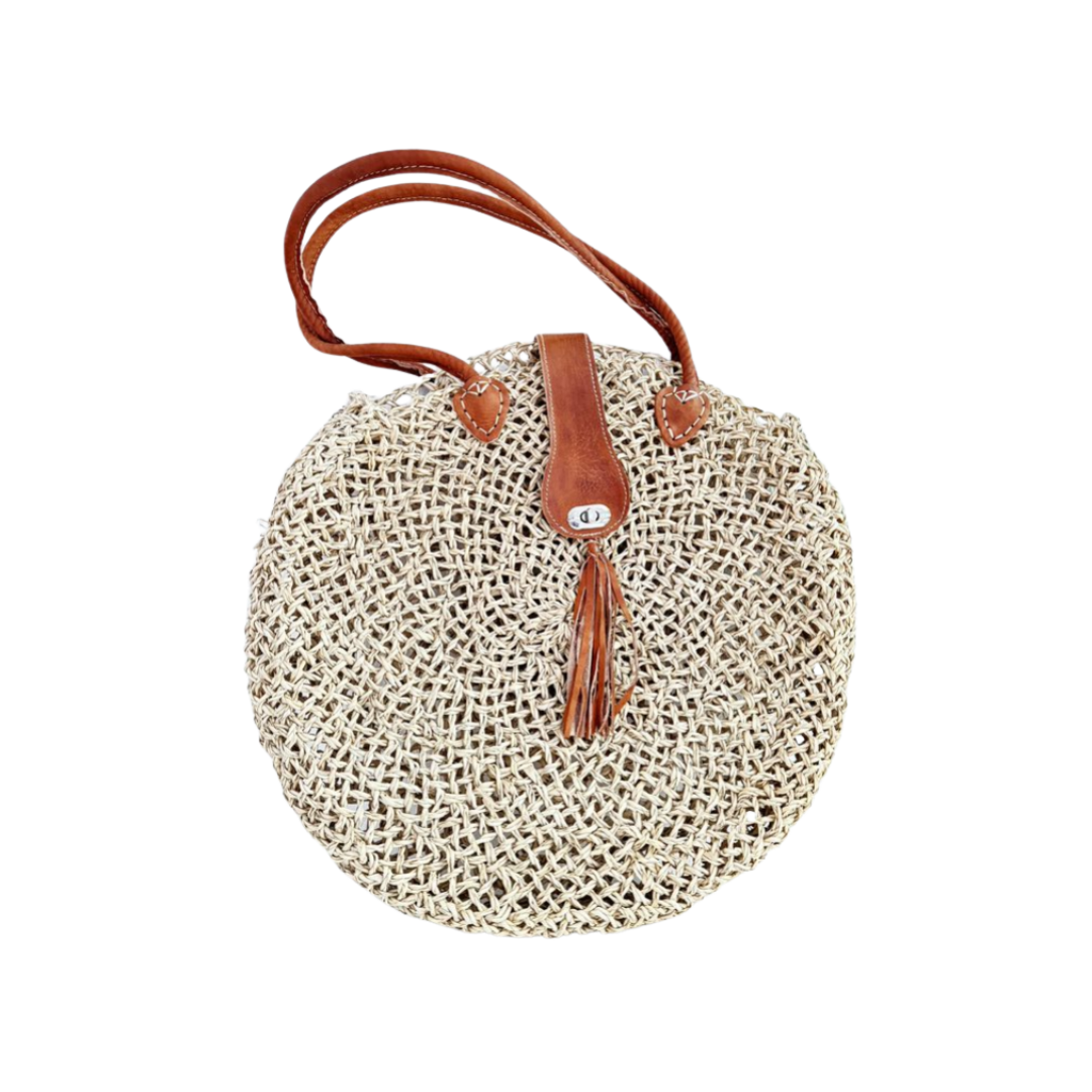 Runde, handgewebte Basttasche aus grobem Raffia mit braunem Lederüberschlag, Quastenanhänger und zwei Lederhenkeln