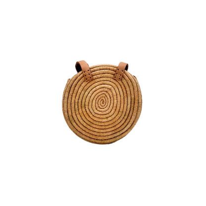 Kleine, runde Basttasche aus handgewebtem Raffia mit zwei braunen Lederlaschen zur Befestigung eines Trageriemens